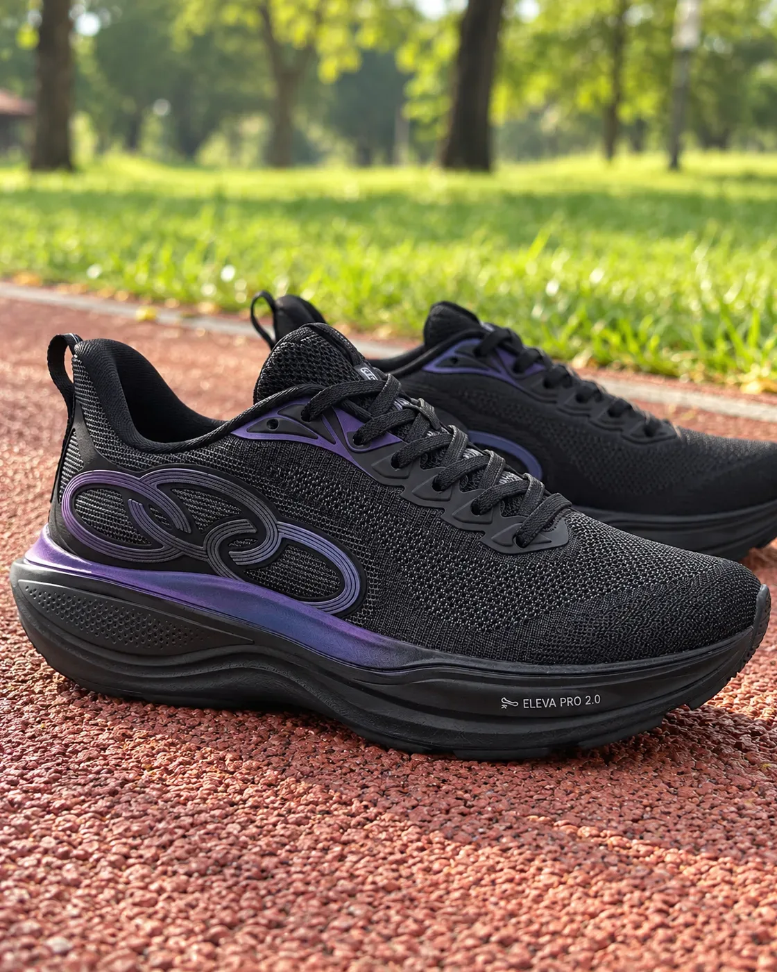 Par de tênis Olympikus Pride 4 preto, com detalhe roxo na lateral, sobre a pista emborrachada vermelha de um parque, com grama e árvores ao fundo